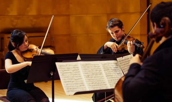 two violinists and a cellist sit playing their instruments