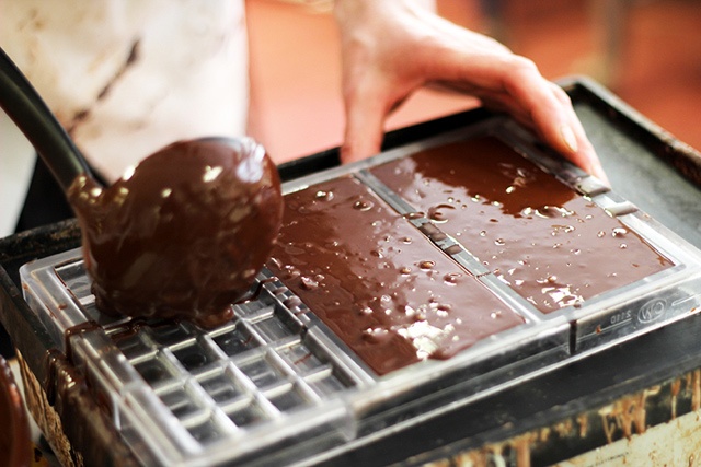 a person fills a chocolate bar mould with melted chocolate