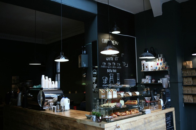 the black interior of coffee shop Artisan Roast with a wooden counter filled with products to eat and drink for sale
