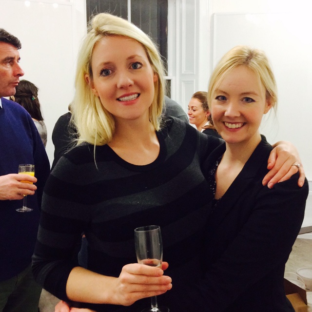 a woman stands holding a glass of champagne with her arm around another woman