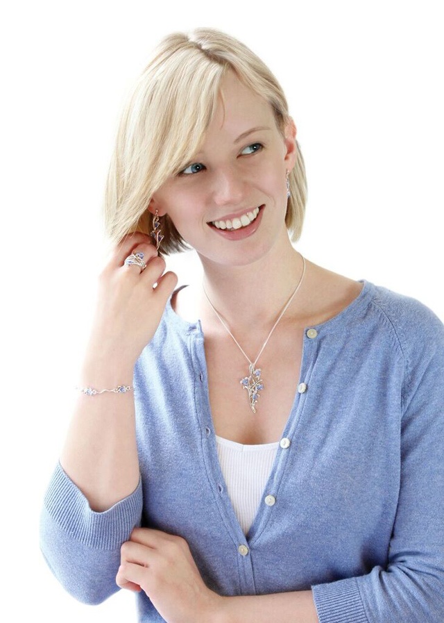 a slim blonde woman stands touching her hair in a blue cardigan and white top