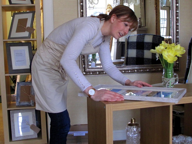 a woman bends over to inspect a picture frame