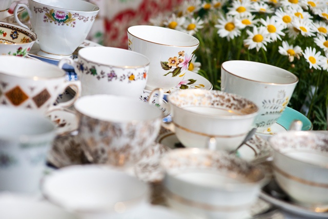 thirteen china tea cups on a table with a vase of daises