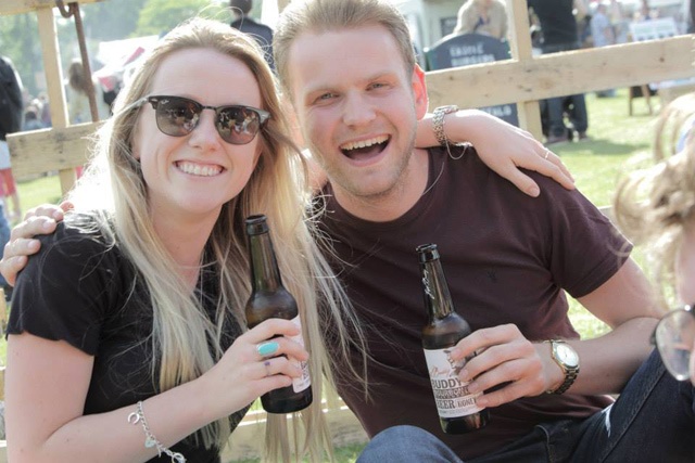a man and woman siting on the ground drinking bottles of beer and smiling