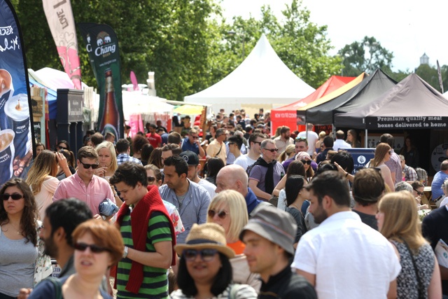 crowds of people walk between stalls at a food festival