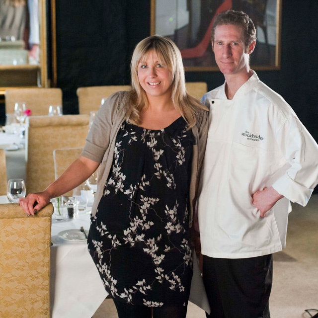 a man and woman stand in the dining room of their restaurant