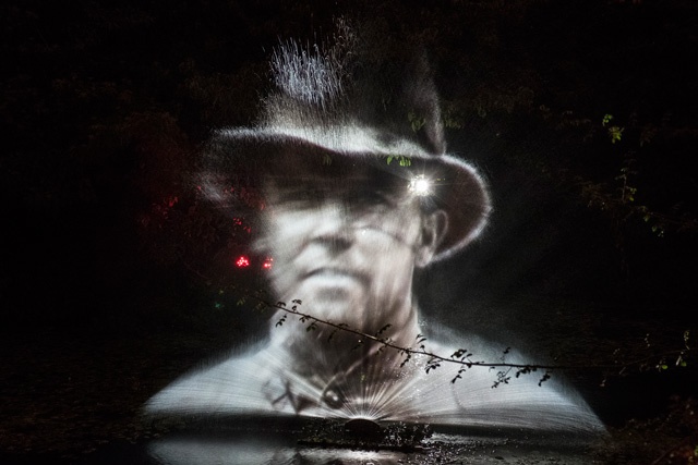 an image of a man wearing a hat projected on to a spray of water at night