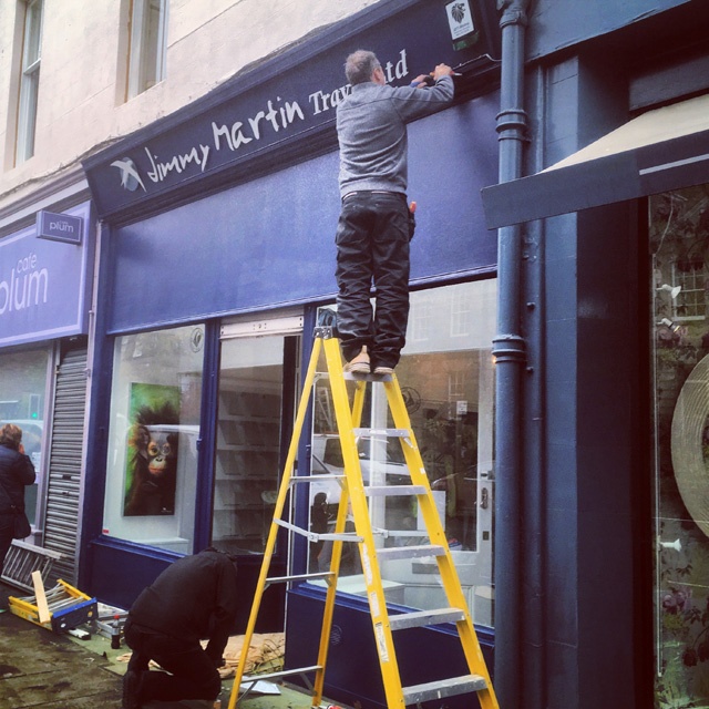 a man stands on top of a yellow ladder installing a sign for a shop
