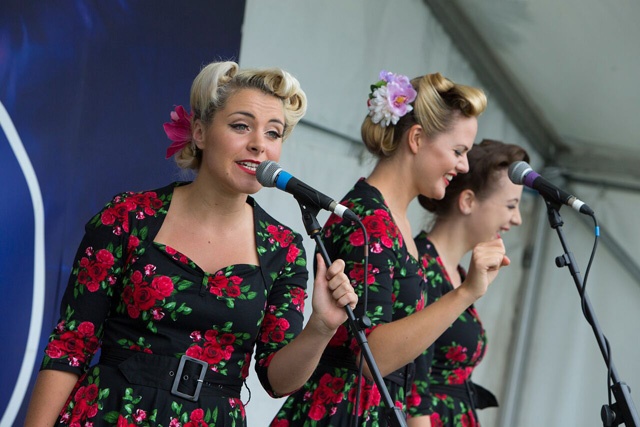 three blonde female singers in matching dresses on stage