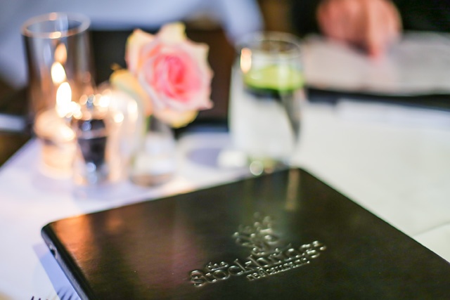 a black leather bound restaurant menu sits on a white linen covered table