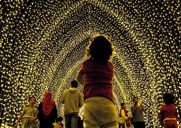 family's stand gazing up at a festive winter tunnel of lights