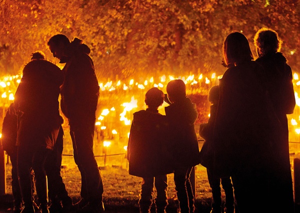 silhouettes of families wrapped up for winter standing in front of a festive fire garden filled with burning torches