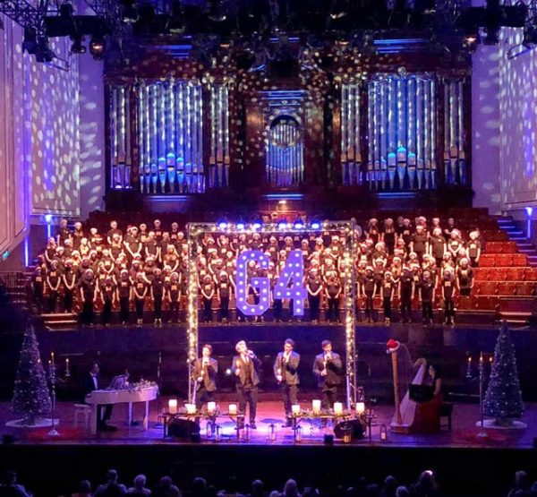 a large Christmas choir of children on stage wearing Santa hats