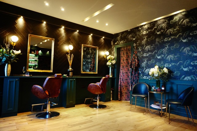 brown leather seats sit on wooden floors in front of gold framed mirrors in a hair salon