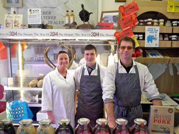 two men and a woman in aprons stand behind the counter in a butchers shop
