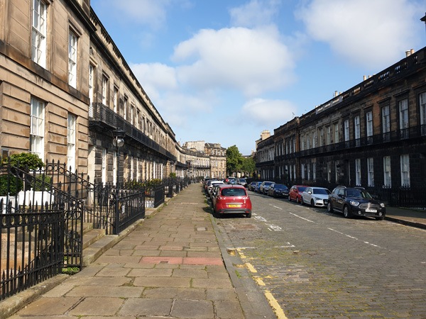 a row of terraced Georgian houses with balconies on each side of a cobbled street