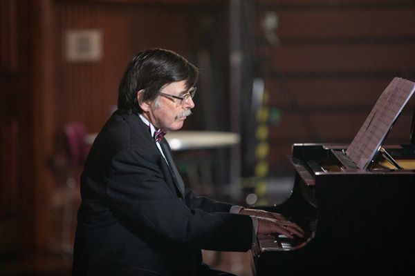 a pianist in a suit and bow tie sits playing at his piano
