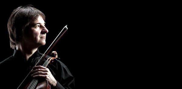 a side profile of a violinist from the Waddell Orchestra in a black shirt on a black background holding his violin close to his chest