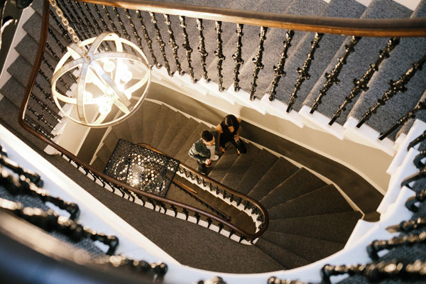 A man and a woman walk up a long winding carpeted staircase in the beautiful Nira Caledonia Hotel in Edinburgh Scotland