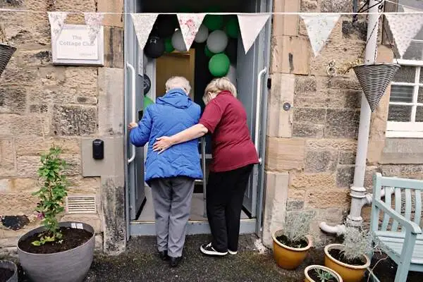 a female LifeCare carer helps an elderly woman through her front door